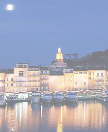 Boats docked at the Port of Saint Tropez at night with light reflections.